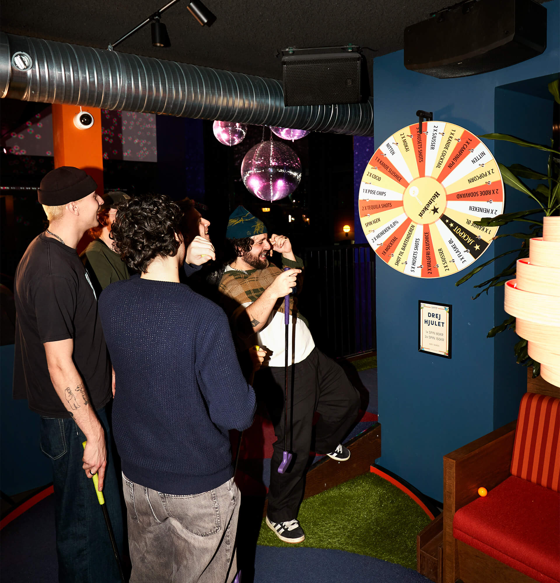 Fire mænd som grinende kigger på et lykkehjul på Camping Bar ved Aaen i Århus.